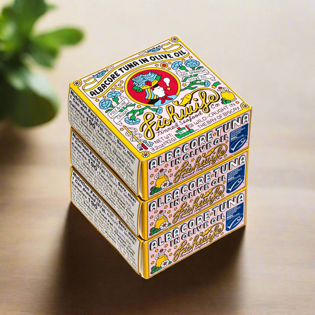 Three stacked fishwife tuna boxes with colorful labels on a kitchen table with green leaf in back