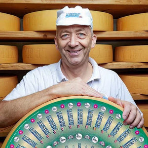 Man holding a wheel of cheese with a background of cheese wheels