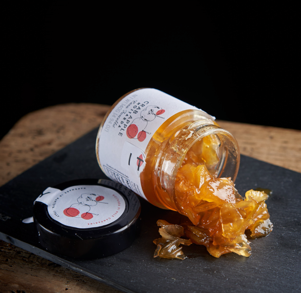 Open jar of Crab apple mustard with a visible brand label on a dark surface