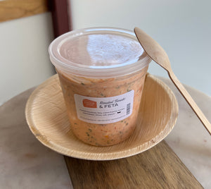 housemade roasted tomato feta in a container, with a palm leaf bowl, on a marble and wood table
