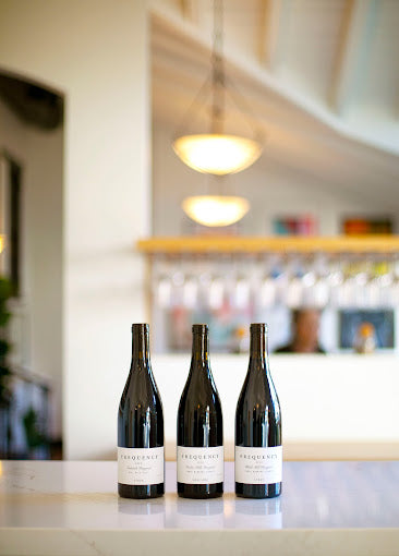 Three bottles of Frequency wine with tasting room in background