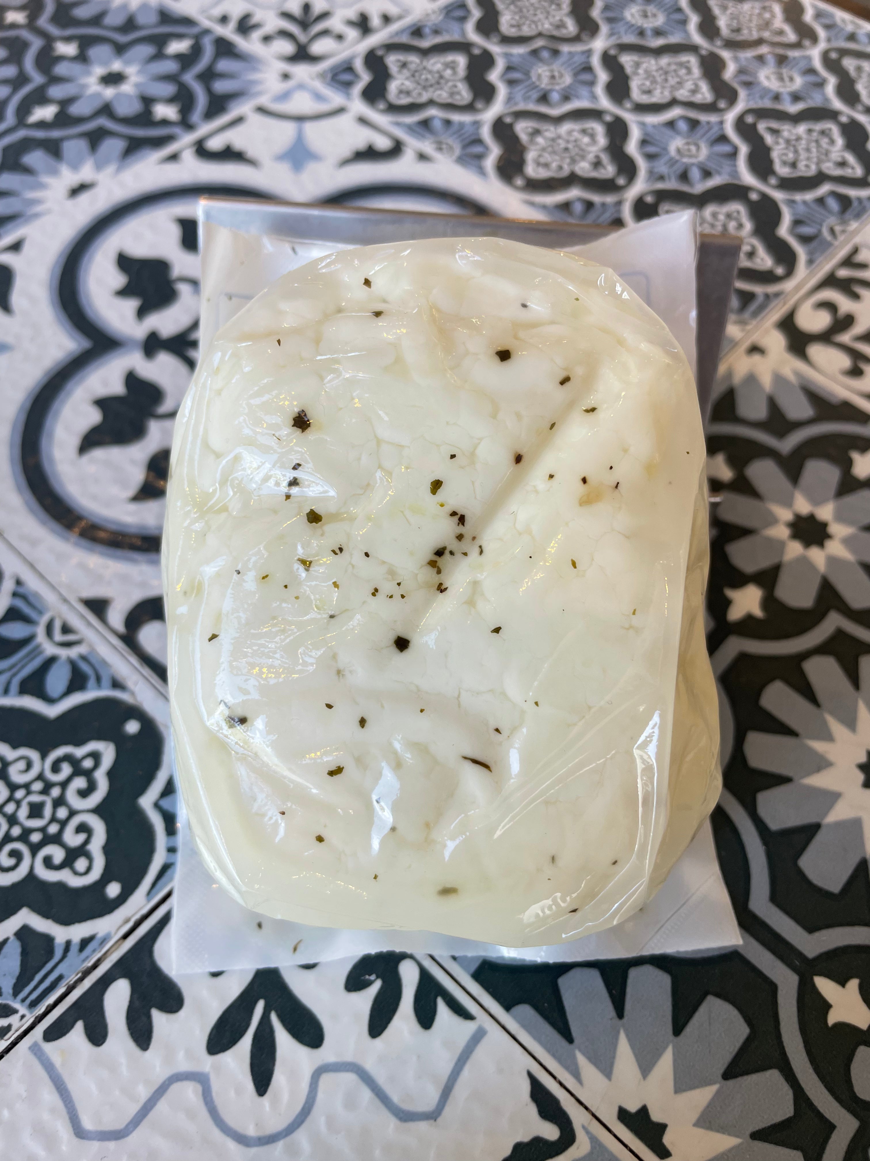 Backside of halloumi (milky white soft cheese with green speckles of mint in vacuum sealed package on a patterned surface