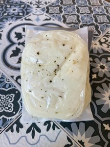 Backside of halloumi (milky white soft cheese with green speckles of mint in vacuum sealed package on a patterned surface