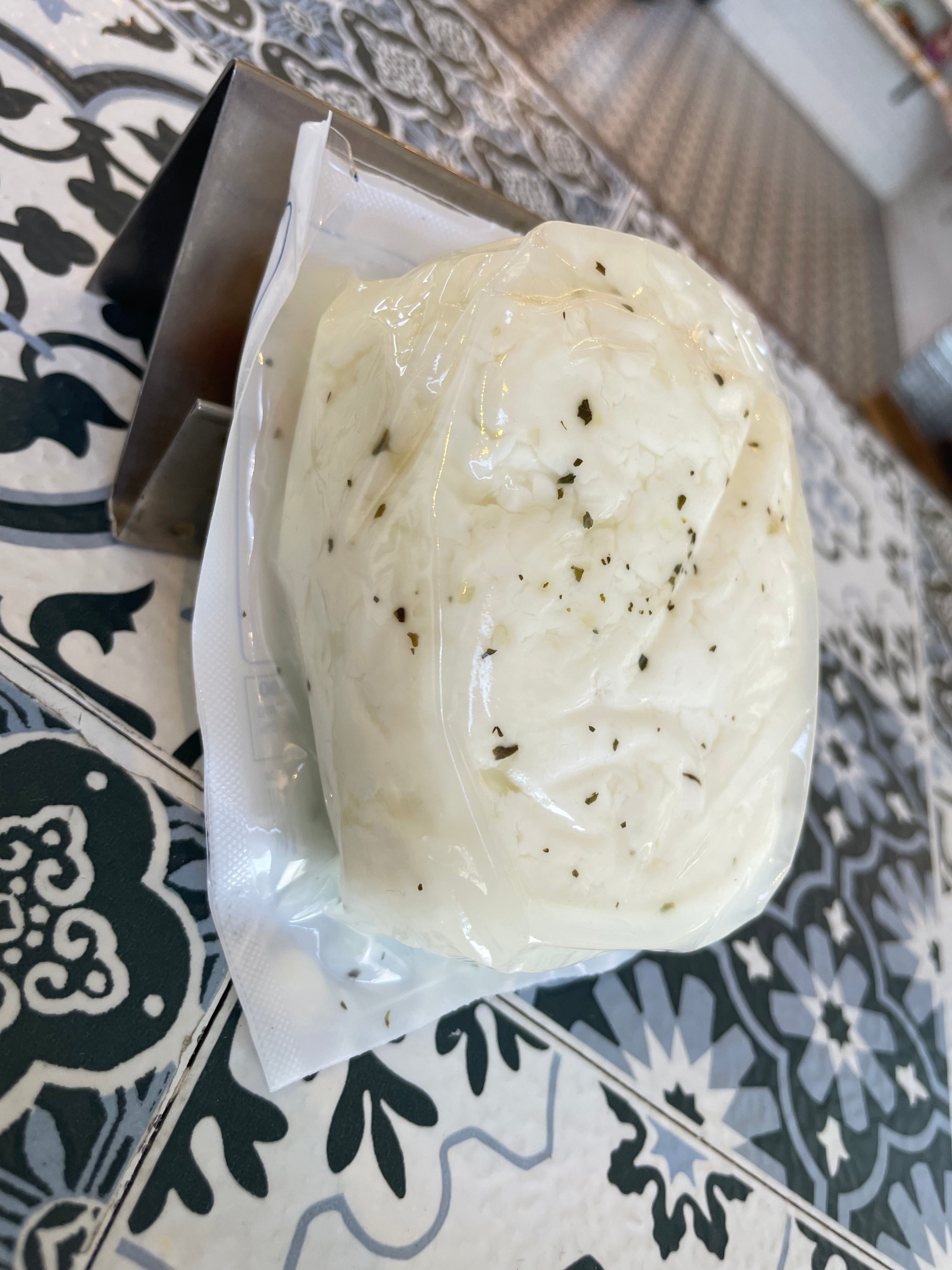 Side angle of halloumi. Milky white rectangular block of cheese with green speckles of mint throughout the surface. vacuum sealed. On a patterned surface.