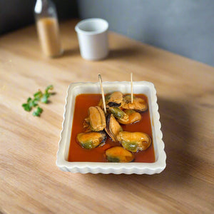 plate of mussels in marinated sauce, ontop of a wooden countertop with toothpicks in them