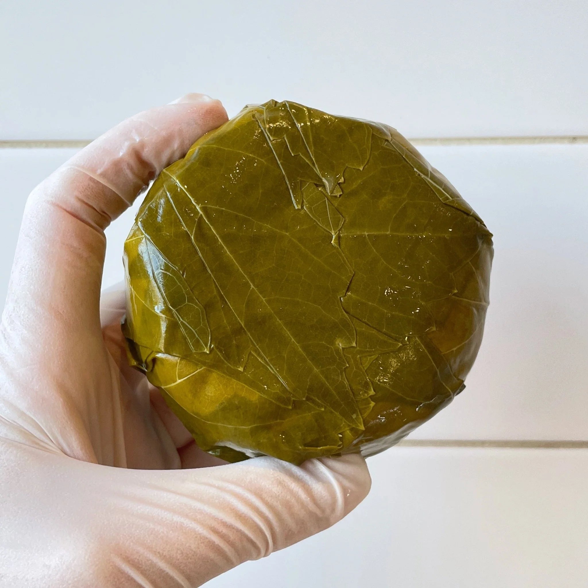 Muscat-soaked grape leaf in round ball, surrounding round cheese