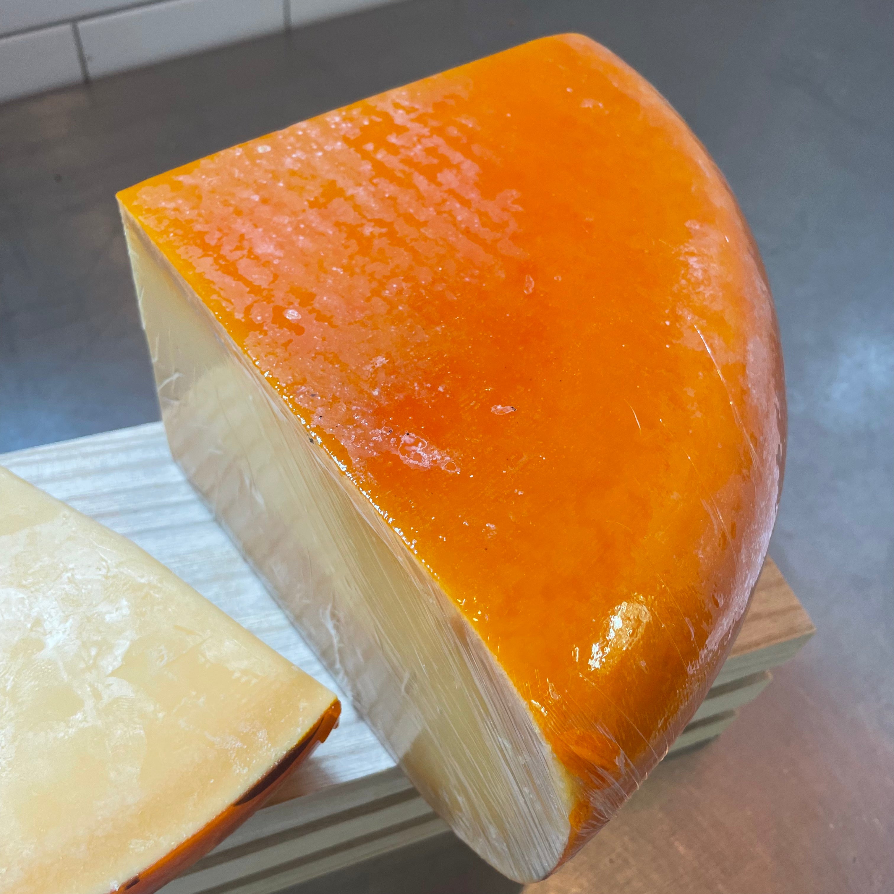 Quarter wheel of pril gouda. Bright orange rind, on a wooden crate 