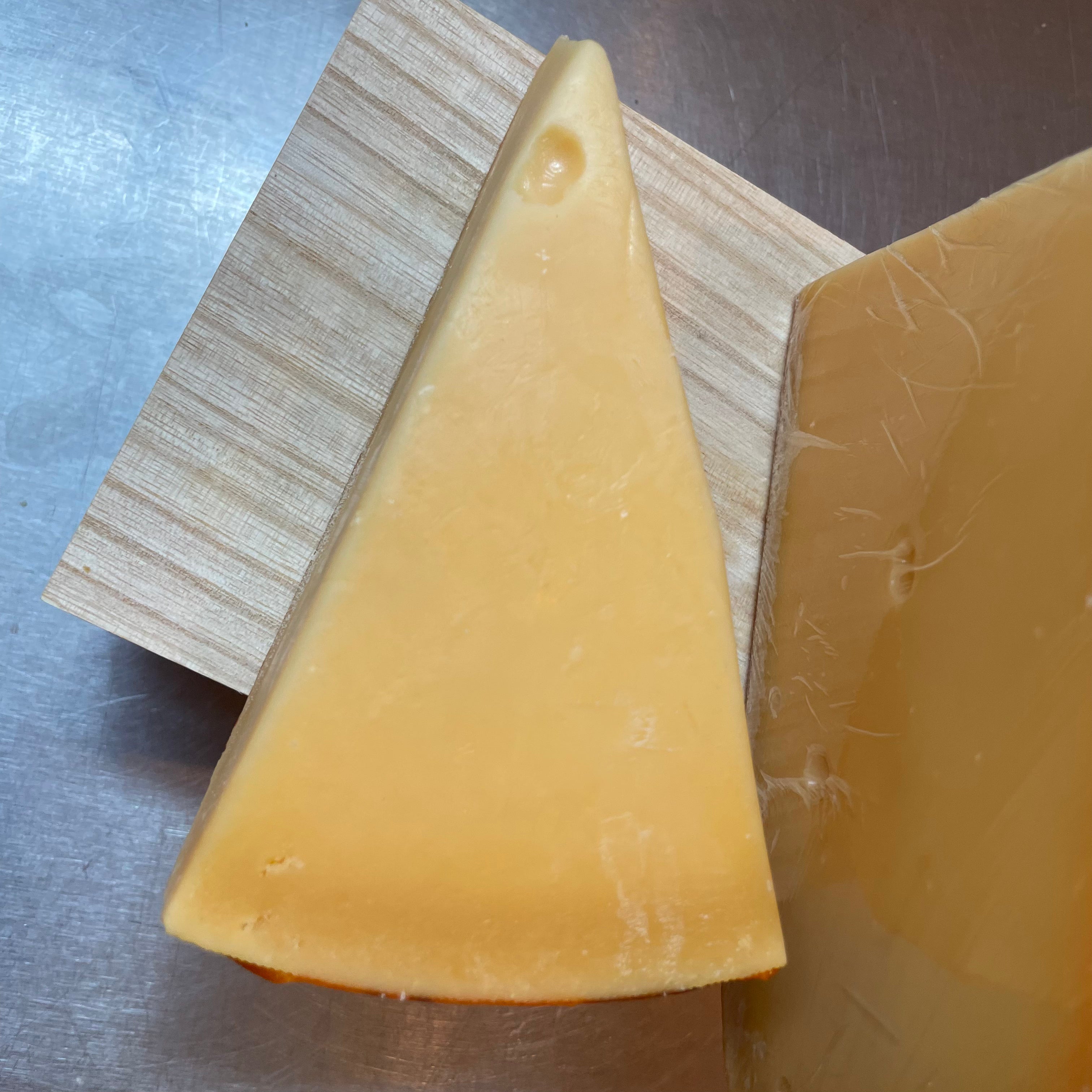 Wedge of cheese with a small hole, pale golden-yellow paste, on a wooden board with a metal surface underneath