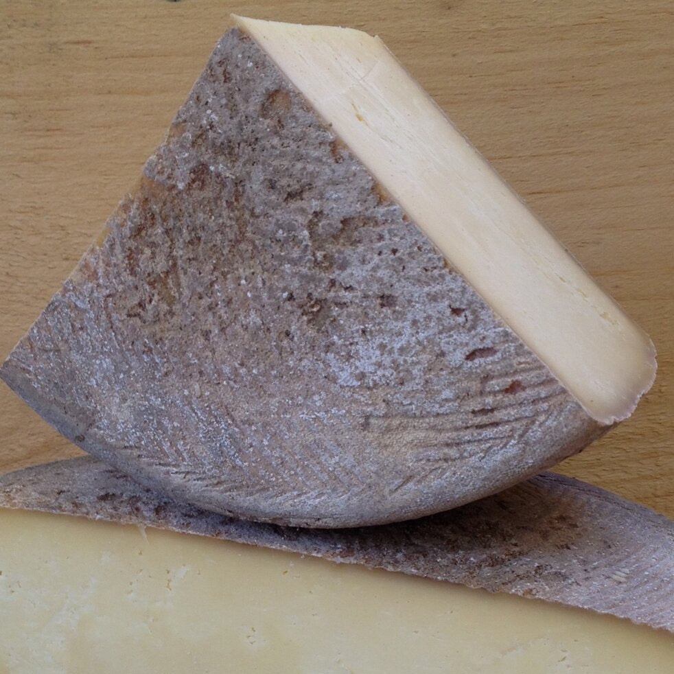 quarter wheel of white paste cheese, with mountain cliff like rind, dark grey/brown