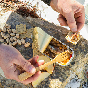 Person preparing a snack with tinned container of sardines on a rocky surface