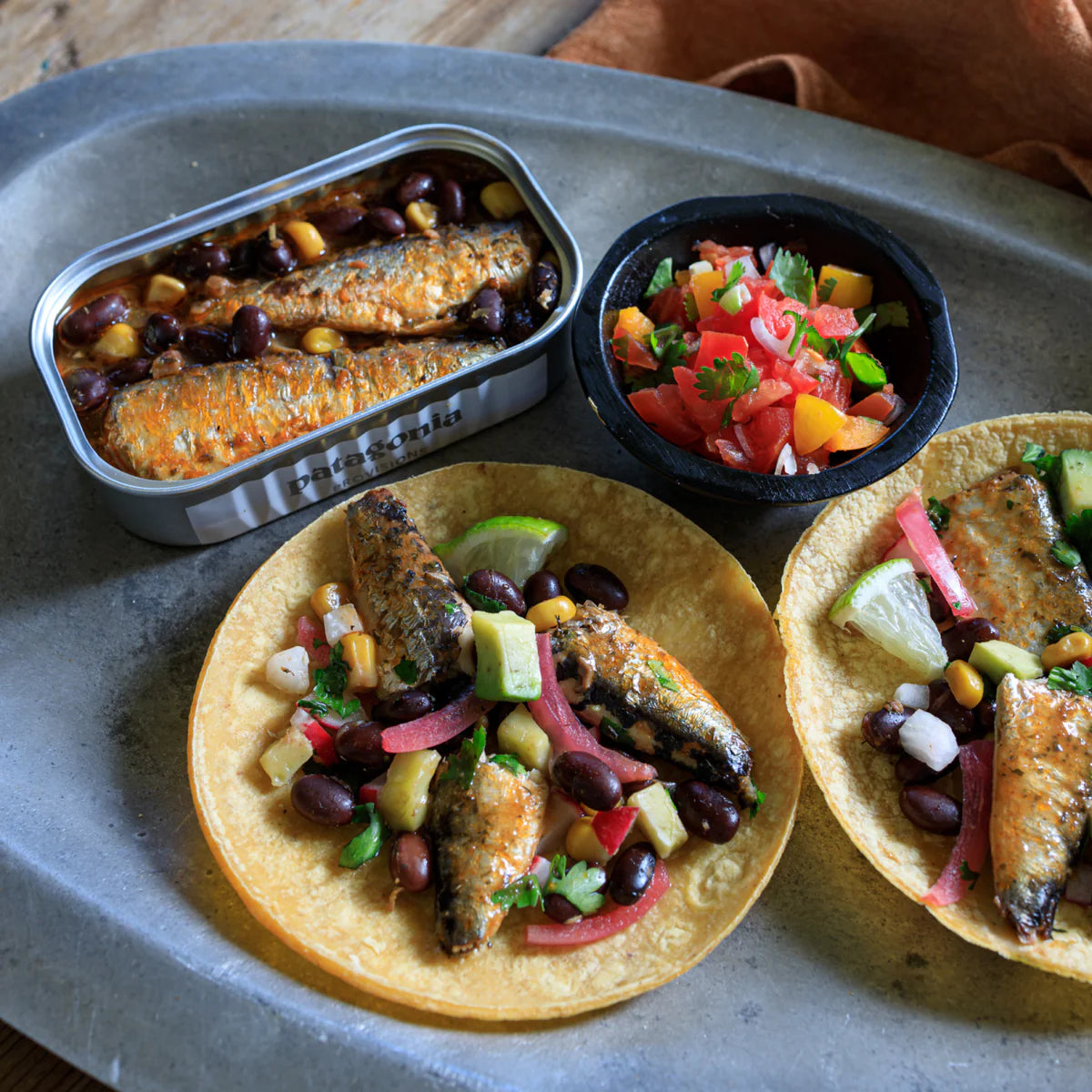 Tacos with fish and vegetables on a tray with a side of beans and salsa.