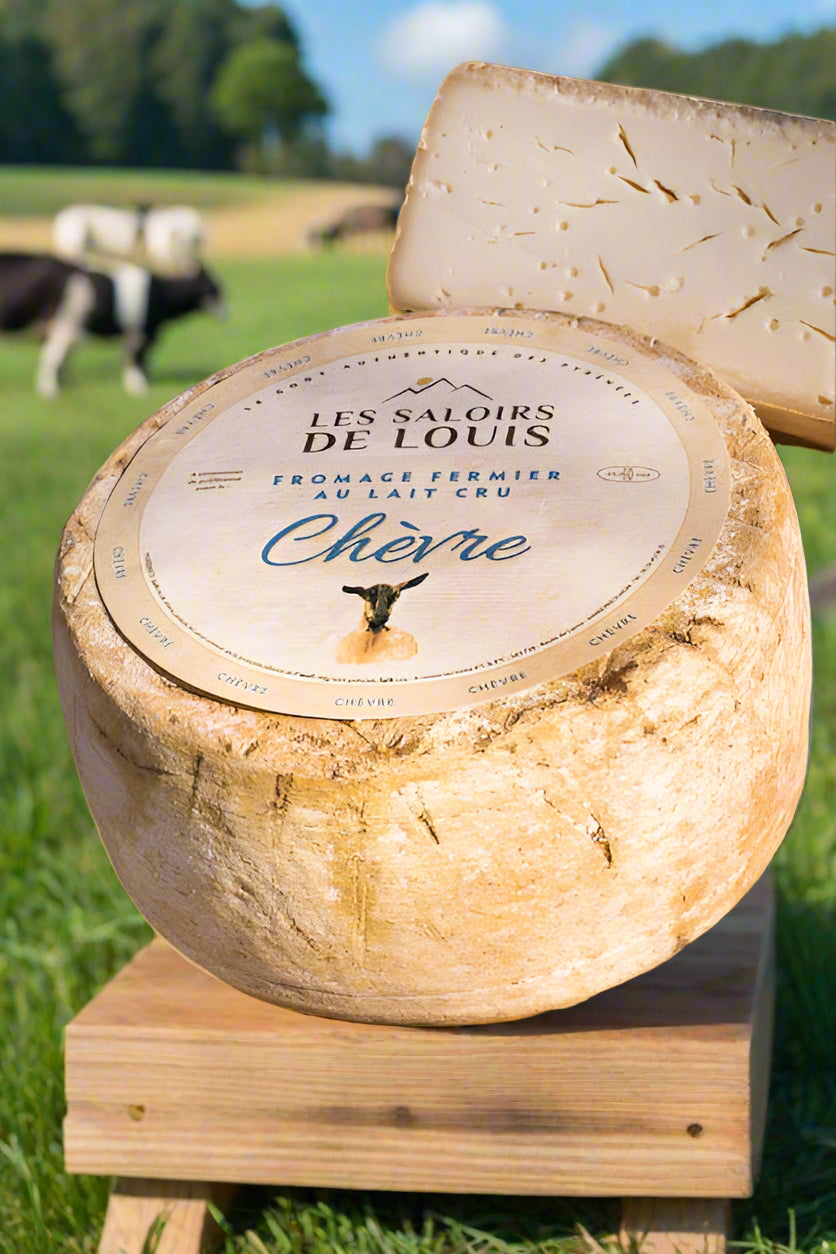 Tomme Fermir full wheel with label showing "les saliors de louis - fromage fermier au lait cru chevre". In green pastures with goats/cows behind. Also showing half wheel with cracks and holes