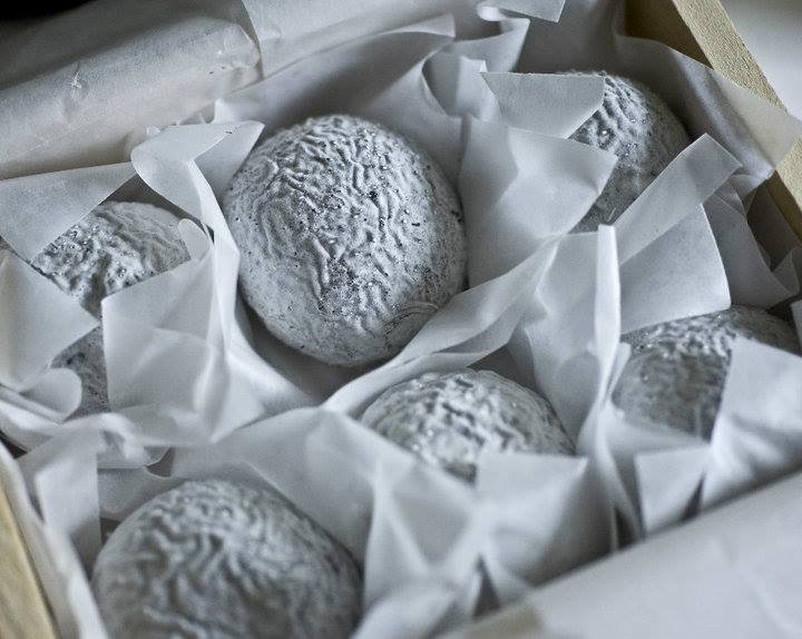 Wrinkly grey/white rinded soft cheese, 6 of them, on wax paper, in a wooden crate