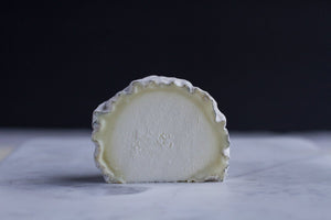 Half of a wheel of wabash cannonball, with a stark white harder center and a goey outer-rind, on a marble surface with a dark background