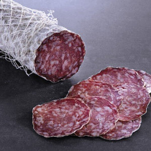 stick of salami with skin-on and netting-on, with slices of the salami in front, stacked