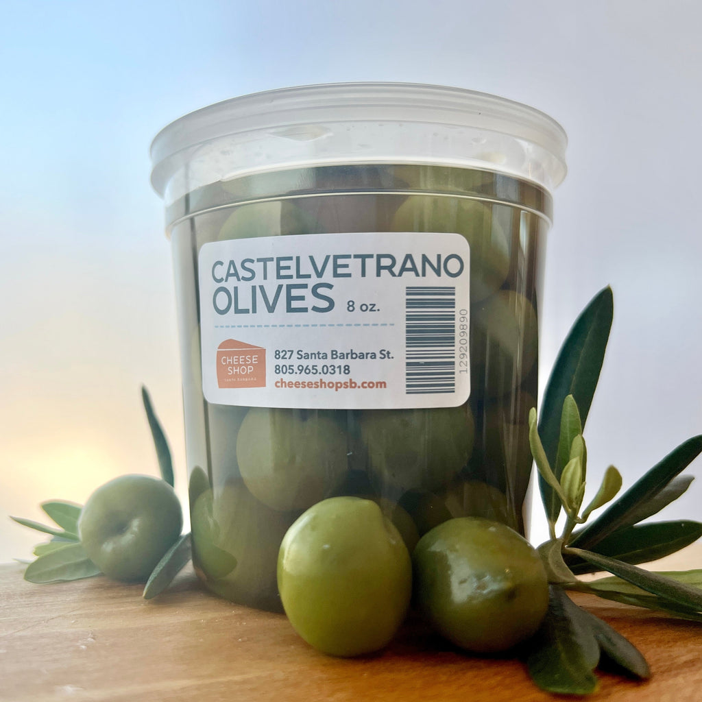 castelvetrano olives in plastic container with olive leaves and branches