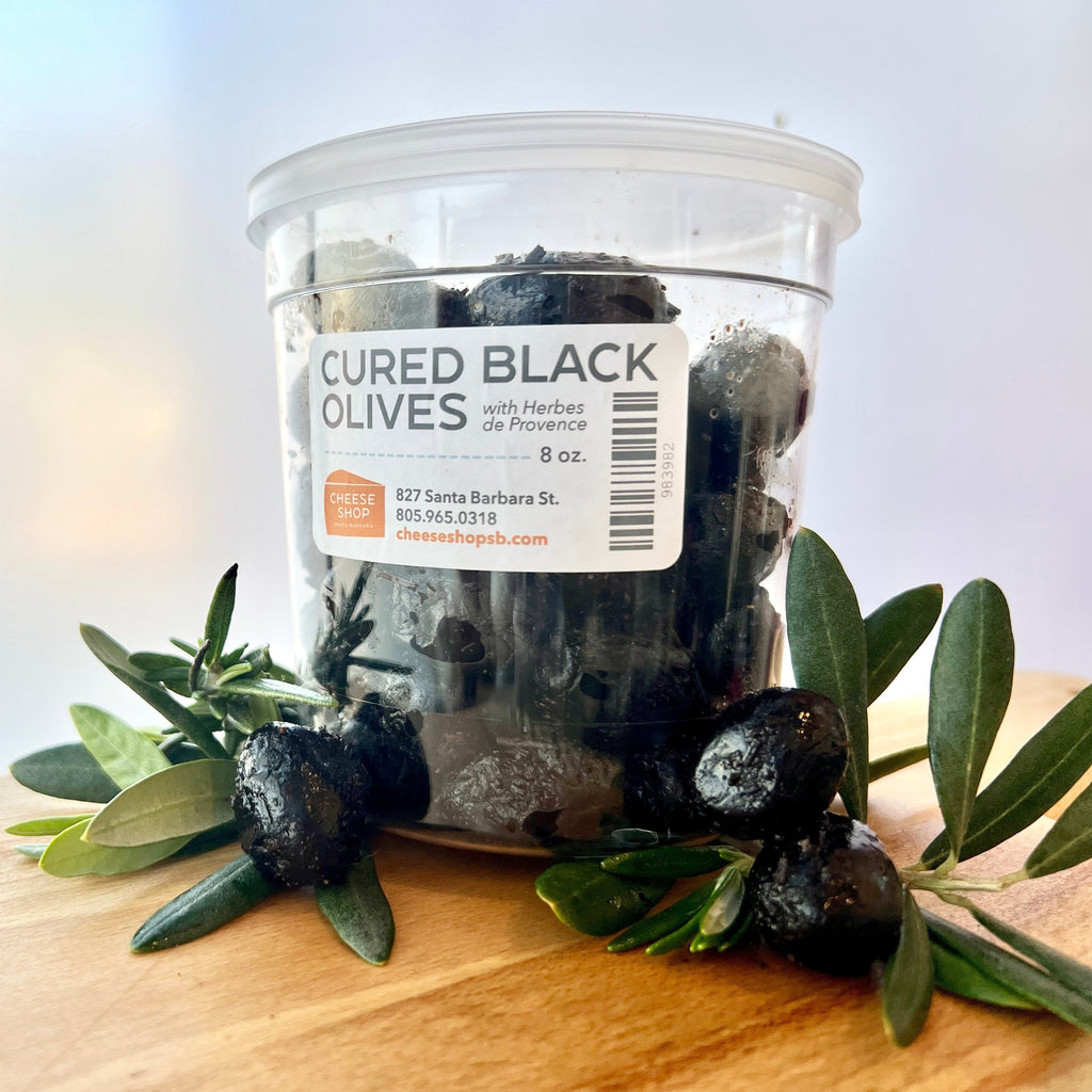 cured black olives in plastic container with olive leaves