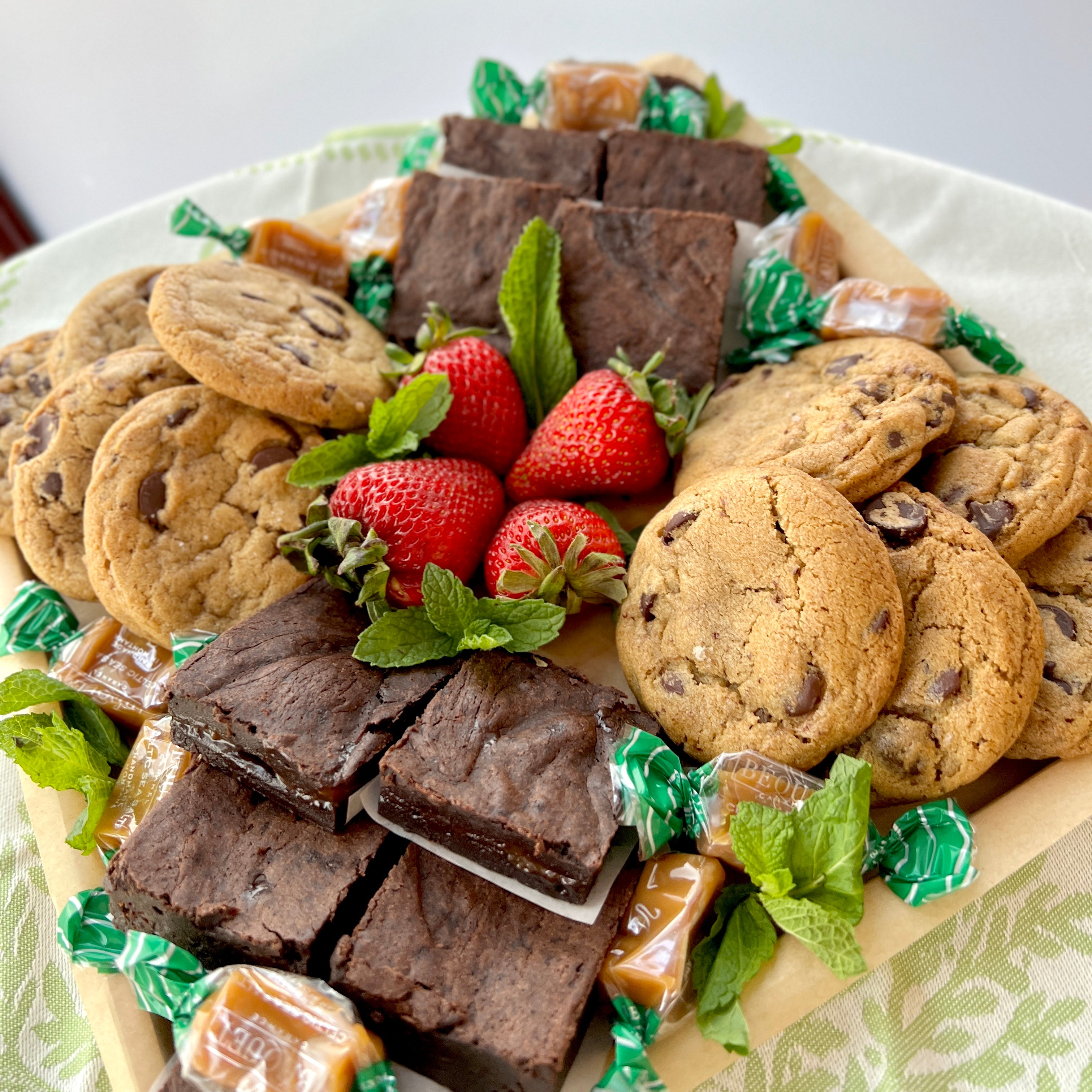 mixed dessert platter with strawberries, brownies, and cookies, and caramels, on square wooden platter
