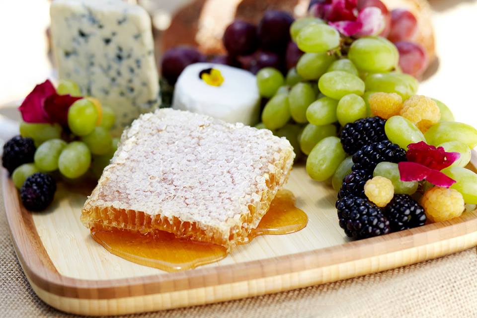 raw honeycomb gooey, on a wooden platter with grapes, blackberries, and blue cheese