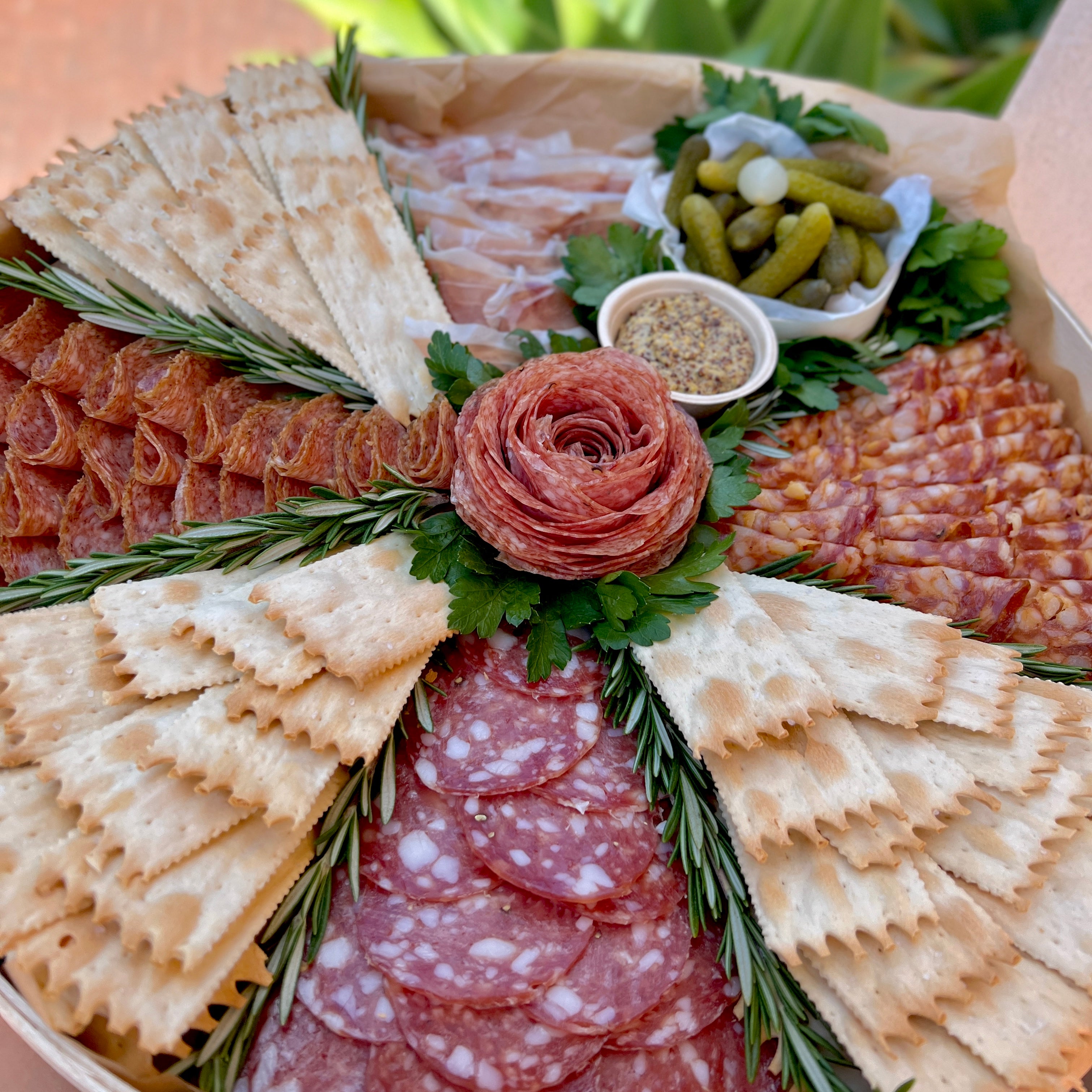 round wooden platter, with salami rose, slices of salami, crackers, cornichons, and mustard