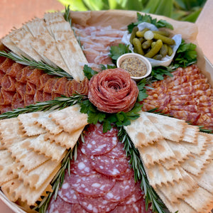 round wooden platter, with salami rose, slices of salami, crackers, cornichons, and mustard